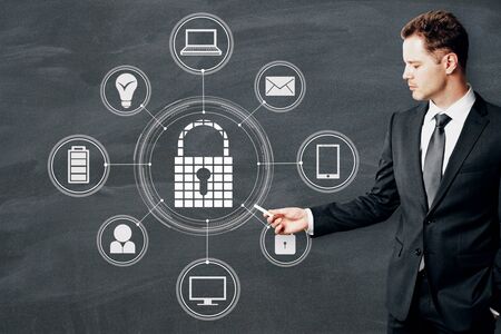 Handsome young businessman drawing creative padlock sketch on chalkboard wall background. Safety and...