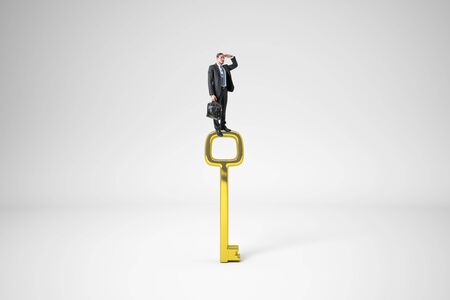 Businessman standing on golden key and looking into the distance on white background. Access and vision conceptの写真素材