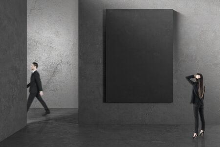 Businessman walking in concrete interior with businesswoman looking at empty billboard on wall. Gallery concept. Mock up,の写真素材