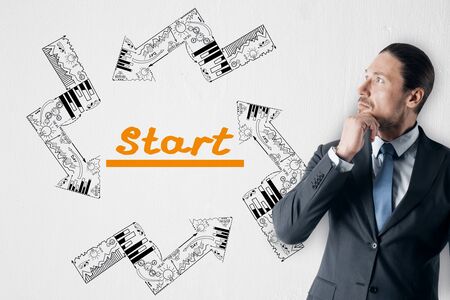 Businessman looking at creative business sketch with text and arrows on white wall background. Startup and success conceptの写真素材