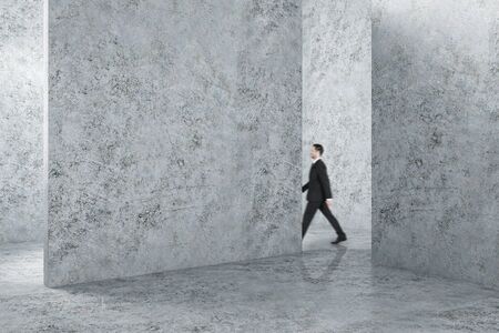 Businessman walking in blank concrete interior with copyspace on wall. Gallery concept. Mock up,の写真素材