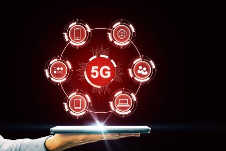Hand using tablet with abstract red 5G interface with computing icons on dark background. Internet...