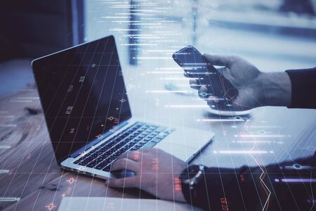 Close up of hands using laptop and smartphone with forex chart on blurry background. Trade and analytics concept. Double exposureの写真素材