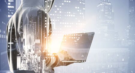 Side view of hacker using laptop on blurry night city background. Malware and technology concept....