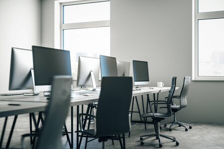 Contemporary blurry grey coworking office interior with equipment and coffee cup on desktop, other...