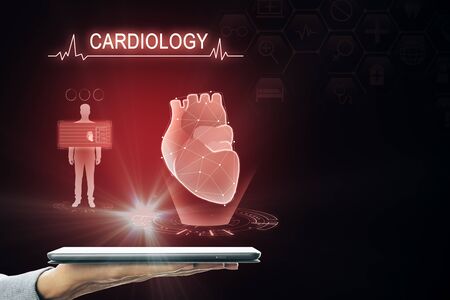 Hand holding tablet with creative glowing red digital heart futuristic interface hologram on dark background. Medicine, cardiology and future conceptの写真素材