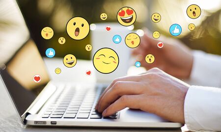 Side view of hands using laptop computer on desktop with emotive smileys on blurry background. Communication and emotion conceptの写真素材