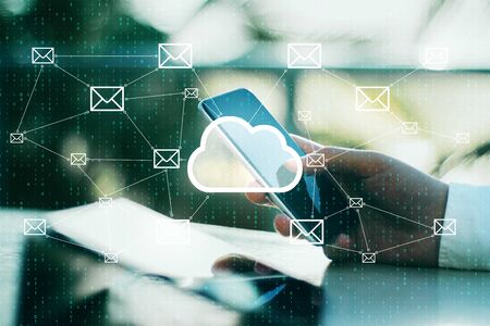 Side view of hands using laptop and cellphone with glowing cloud icon interface on blurry background with email letters. Cloud computing and communication concept. Multiexposureの写真素材