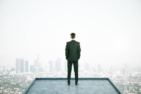 Rear view of businessman looking into the distance on rooftop with daylight city view. Copy space. Success, vision and future conceptの写真素材