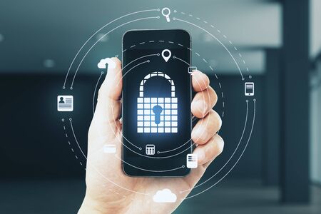Close up of hand holding smartphone with glowing padlock hologram on blurry interior background. Password and network concept. Multiexposure の写真素材