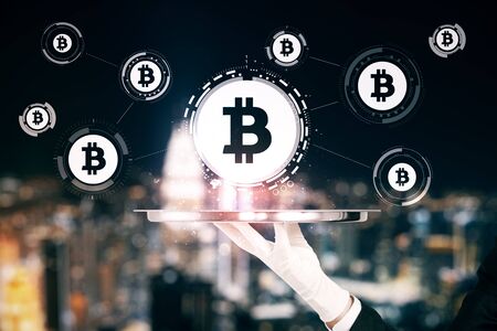 Hand holding abstract glowing bitcoin interface on blurry night city background. Cryptocurrency and...