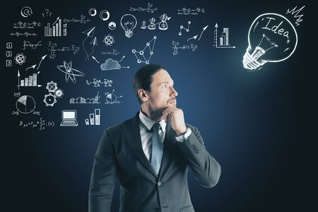 Success and technology concept. Portrait of attractive thoughtful young businessman standing on dark wall background with business sketch の写真素材