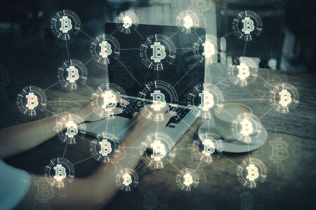 Close up of hands using laptop on desktop with coffee cup glowing bitcoin hologram. E-commerce and payment concept. Multiexposure の写真素材