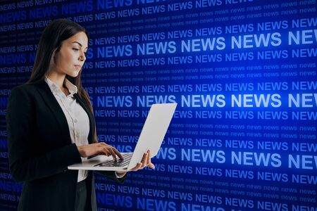 Attractive young european businesswoman with laptop and creative blue news hologram on dark background. Information and media conceptの写真素材