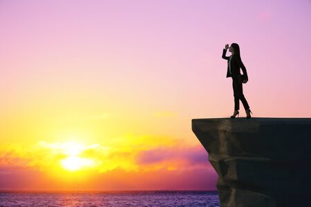 Leadership and research concept. Side view of backlit businesswoman standing on cliff and looking...