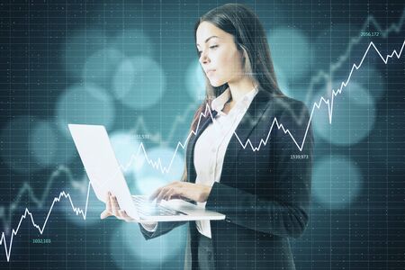 Businesswoman with laptop and stock data hologram. Trade and currency concept.の写真素材