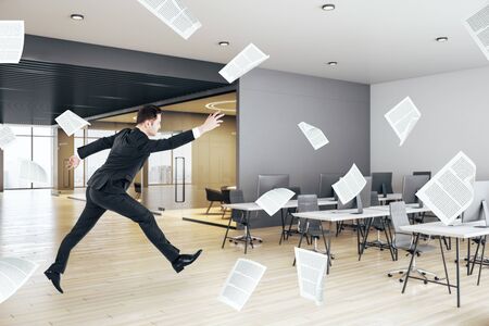 Businessman jumping in contemporary concrete office interior with city view. Management and paper work conceptの写真素材