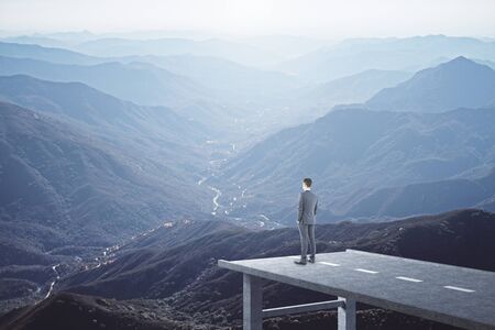 Businessman standing on road and looking to mountain landscape. Success and startup concept.の写真素材