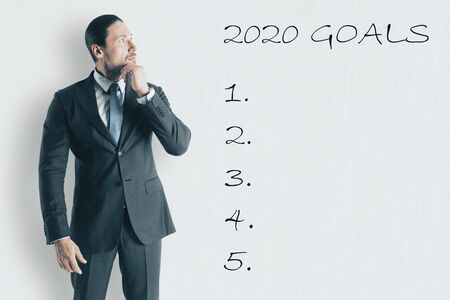 Businessman thinking and looking on drawing 2020 goals list on white wall. Success in 2020 year conceptの写真素材