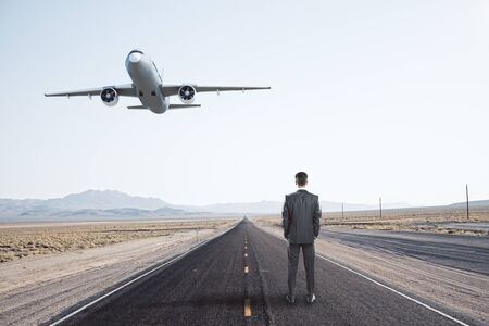 Businessman standing on road and passenger airplane flying in the blue sky. Travel and vacation conceptの写真素材