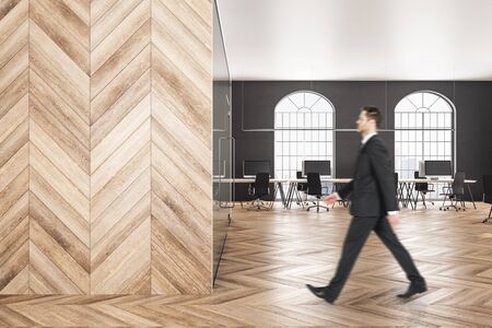 Attractive young businessman walking in wooden office. Executive and research concept.の写真素材