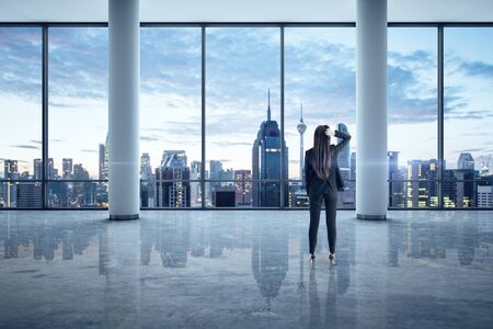 Businesswoman standing in empty office interior with megapolis city view. Business and success concept.の写真素材