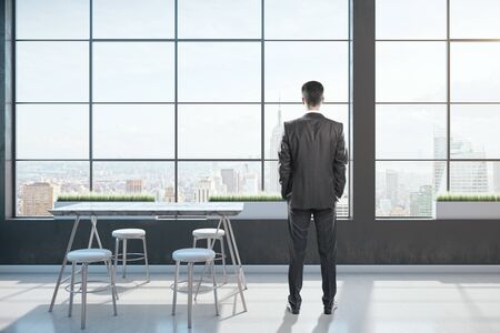 Businessman in clean freelancer space interior with table and panoramic megapolis city view.  Occupation and worker conceptの写真素材