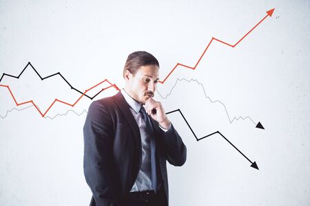 Thinking businessman standing near gray wall with drawing arrows. Leadership and success conceptの写真素材