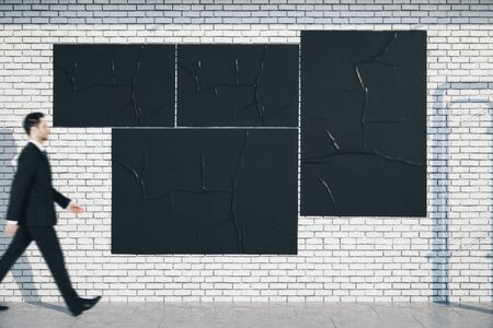 Businessman walking near blank three black posters on loft style brick wall. Presentation concept.