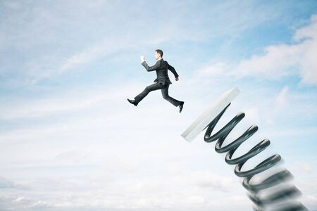 Businessman lauching off big spring on sky background with clouds. Startup and success conceptの写真素材