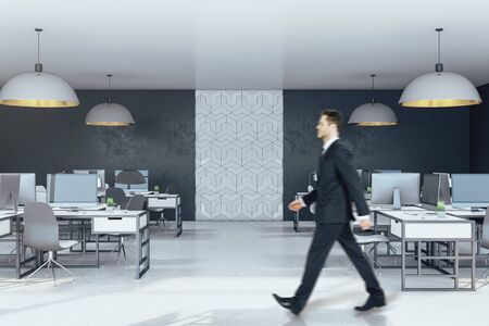 Businessman walking in office interior with computer on desktop. Occupation and worker concept.の写真素材