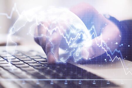 Hand using laptop and recession chart with digital earth hologram. Global business and technology...
