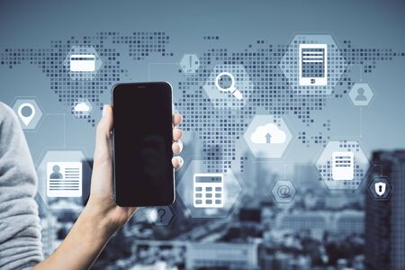 Hand holding smartphone with digital business interface on blurry city background. Technology and innovation concept. Multiexposureの写真素材