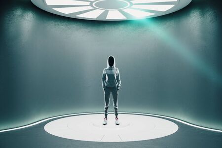 Hacker standing in futuristic gray hall with luminous disc on ceiling. Future and design concept. Mock up.の写真素材