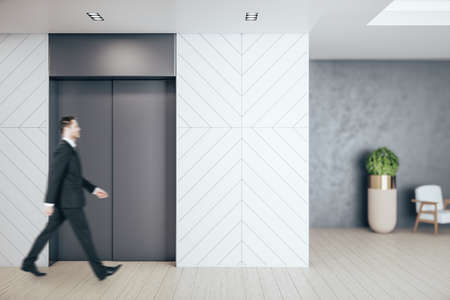 Businessman walking in office hall with elevator, furniture and daylight. Workplace and lifestyle...
