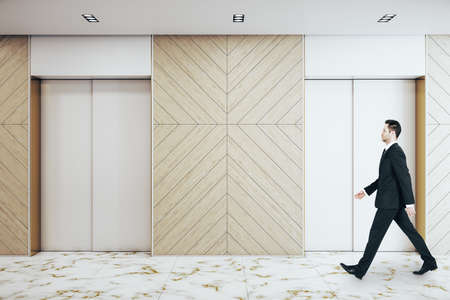 Businessman walking in office hall with two elevators, furniture and daylight. Startup and...