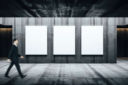 Businessman walking in gallery interior with three empty banners concrete wall. Museum and exhibition concept.の写真素材