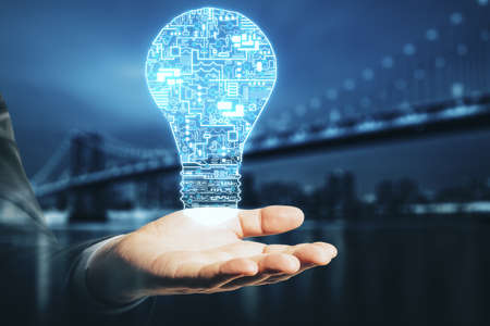 Hand holding creative glowing digital circuit lamp on dark city background. Technology and startup...
