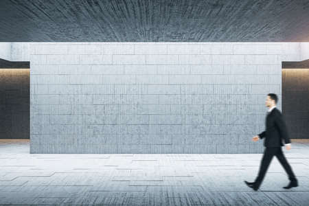 Businessman walking in minimalistic brick gallery interior with empty gray wall. Museum and exhibition concept. Mock up,の写真素材