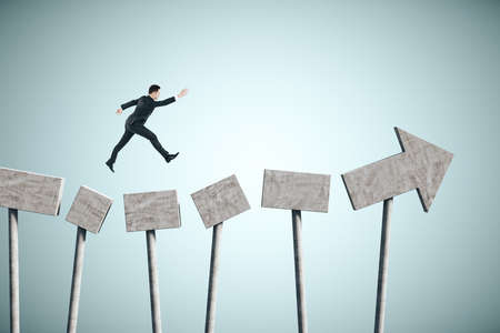 Businessman jumping on concrete arrow on gray background. Growth and forward concept