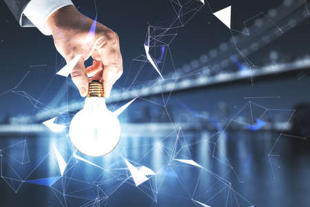 Hand holding creative polygonal light bulb on city background. Innovation, technology and solution conceptの写真素材