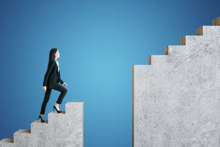 Businesswoman in suit walking on intermittent staircase on blue background. Success and challenge conceptの写真素材