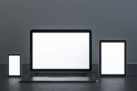 Laptop, digital tablet and smartphone with blank white screen on concrete table. Technology and...