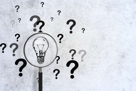 Magnifying glass search light bulb and drawing question mark on concrete wall. Success and startup...