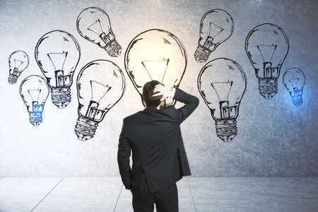 Thinking businessman looking on drawing lamps on conceret wall. Brainstorm and innovation conceptの写真素材