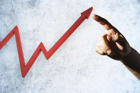 Hand pointing on growing red arrow on concrete wall. Leadership and challenge concept. Close up