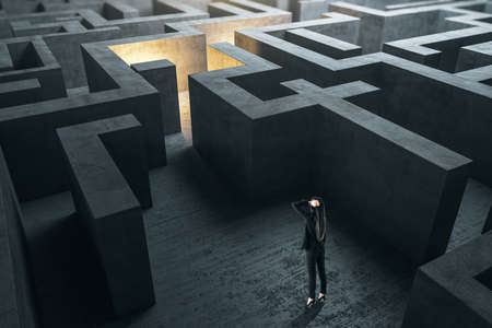 Young businesswoman in suit standing in concerete gray labyrinth. Business and challenge concept.の写真素材