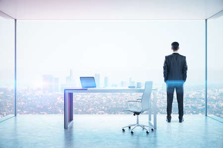 Businessman standing in board room with laptop on table and modern city view. Workplace and worker concept.の写真素材