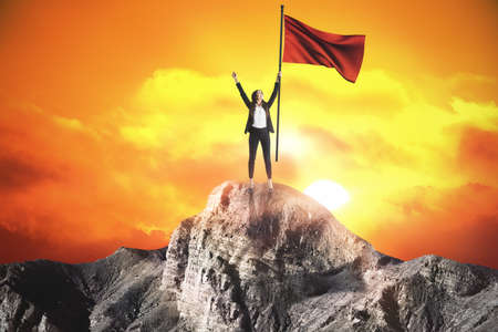 Happy businesswoman with red flag standing on sunset background. Leadership and success conceptの写真素材