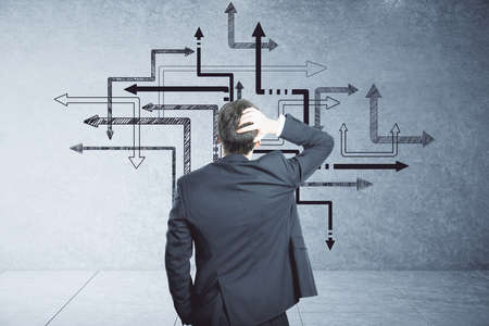 Thinking businessman looking on group arrows drawing on concrete wall. Leadership and way conceptの写真素材